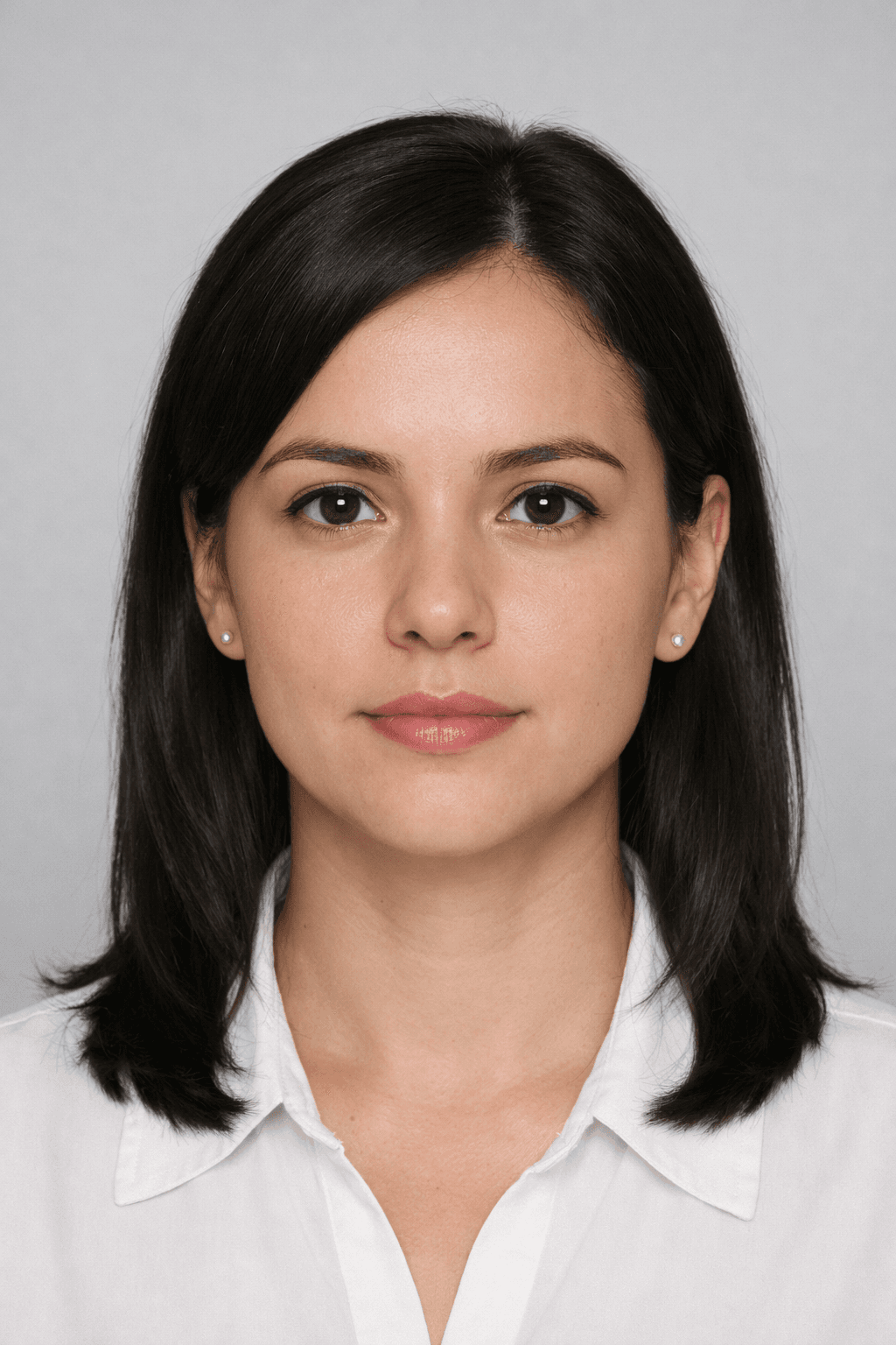 Woman with dark hair and brown eyes wearing a white shirt against a gray background.
